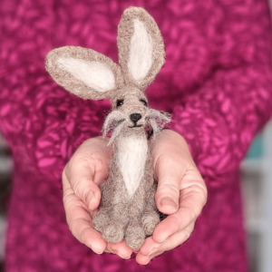 Image of a grey needle felted hare being held in someone's hands.