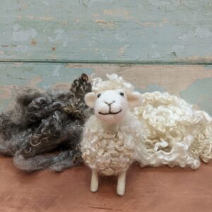 Image shows lovely curly wool locks used for needle felting. Standing next to the wool is a cute, white needle felted sheep that has a topcoat of the same curly wool locks in the photograph.