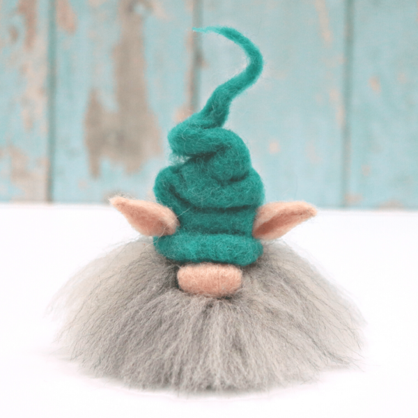Image shows cute needle felted gnom with a big grey and white beard, big nose, and crooked teal coloured hat.