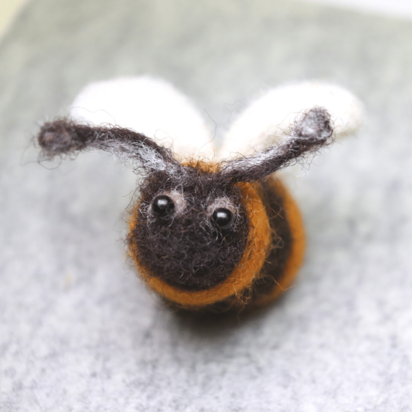 Photograph shows a cute needle felted bumble bee an a grey mottled background.