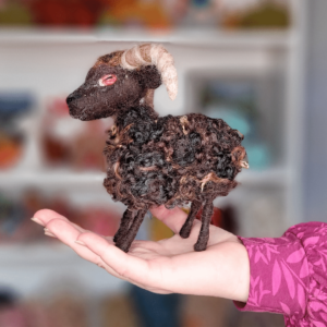 Image shows a needle felted brown Hebridean sheep sat on the palm of a hand